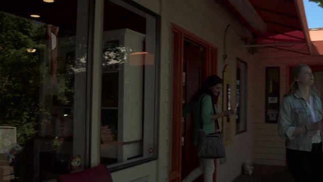 Medium wide shot of two women walking out of a pastry shop