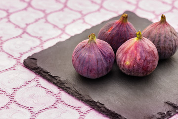 Fototapeta premium Four fresh purple Figы on black slate plate on purple lace tablecloth 