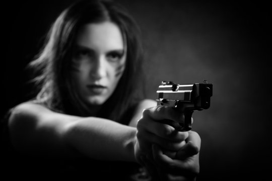 serious young woman with gun aiming on dark background, monochrome