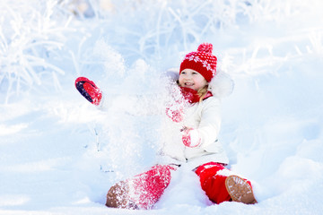 Child playing with snow in winter. Kids outdoors.
