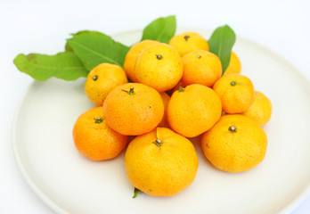 Orange fruit with leaves on white plate isolated on white background.