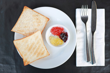 Toast with jam on white plate on the black table.