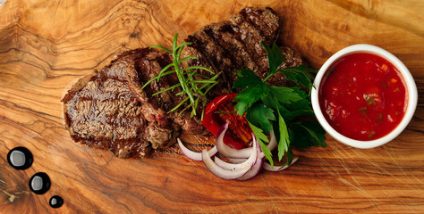 Grilled pork ribs, tomato sauce and green herbs on wooden background, top view