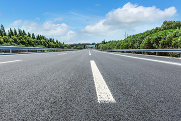 Fototapeta premium asphalt road and green forest under the blue sky