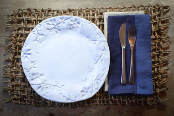 White handmade plate with blue napkin on a rustic woven mat holiday dinner background
