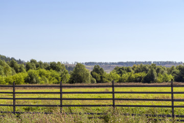 Fototapeta na wymiar Rustic wooden fence against the background of a green field and trees.