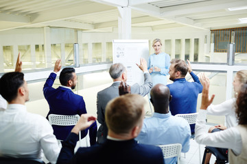 Attendants of business seminar raising their hands to answer coach question after presentation