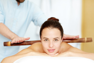 Obraz na płótnie Canvas Calm brunette enjoying massage made up with wooden stick in day spa salon