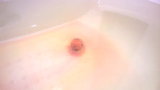 Bath bomb lies on the bottom of the white tub and slowly dissolves. The view from afar. Blurry
