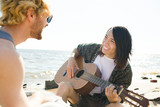 Young guys enjoying guitar music and singing on the beach on summer day