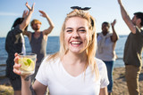 Ecstatic girl with glass of citrus cocktail enjoying gathering with friends on the beach