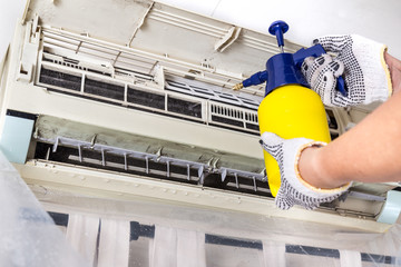 Technician spraying chemical water onto air conditioner grid to clean