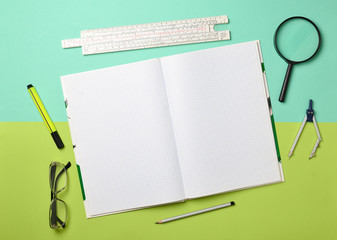 A large notebook for notes and drafting with stationery objects for a student on a green blue...
