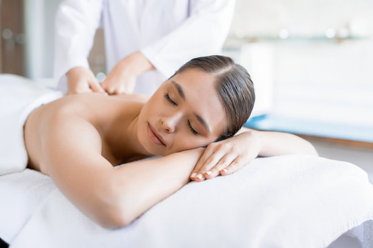 Serene female lying in spa salon and having her back massaged