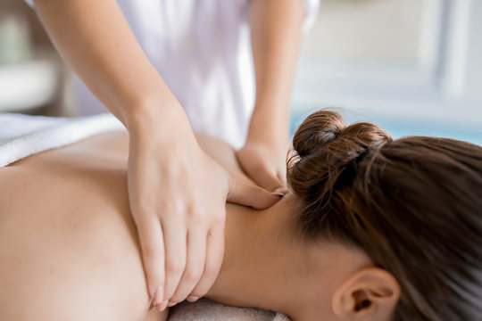 Hands of masseuse massaging neck and shoulders of relaxed client in spa salon