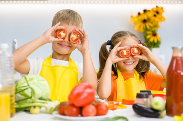 Happy kids having fun with food vegetables at kitchen holds tomatoes before his eyes like in glasses