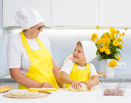 Happy grandmother teaches the child to knead the dough in the kitchen