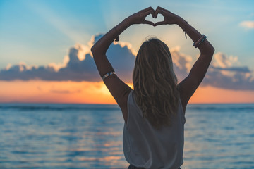 Girl holding a heart shape on the ocean / sea shore.