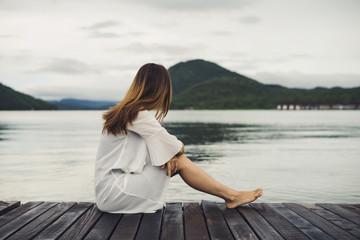 Fototapeta na wymiar Lonely woman sitting on wooden pier and looking at the lake