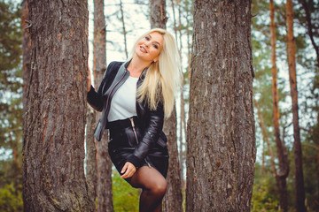 Fashion woman walking in autumn park. Cute woman in nature scenery. Glamorous woman wearing leather jacket and shirt