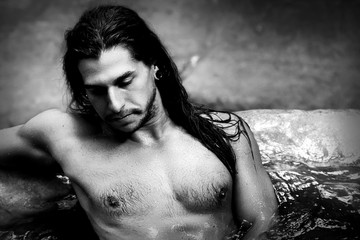 A handsome guy with long hair and piercings on waterfalls in a rain forest. Tarzan concept. Black and white photo.