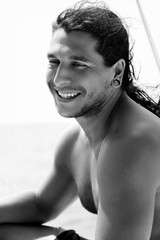 A young handsome sports guy with long hair smiling on the deck of a tourist boat. Black and white photo.