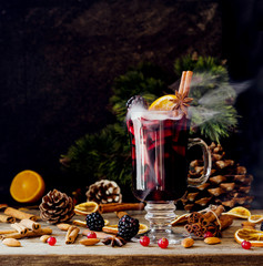glass of hot mulled wine for the new year with ingredients for cooking, nuts and Christmas decorations