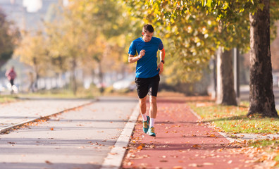 Fototapeta premium Young man wearing sportswear and running at quay during autumn