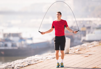 Young man wearing sportswear skipping rope at quay during autumn
