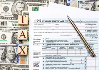 Word "tax" written by wooden cudes with tax form and pen on background of dollar bills. Business concept.