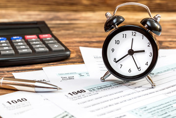 Tax forms with clock, pen and calculator on the office wooden table. Top view. Business and tax concept.