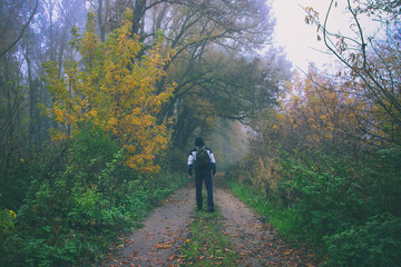 Obraz premium Man with backpack walking in the forest path and looking to the misty woods, travel into autumn nature