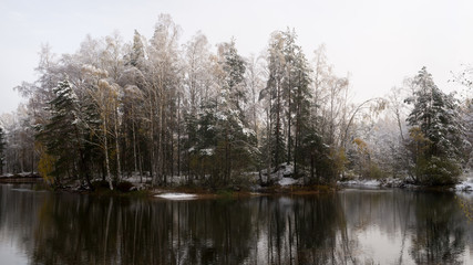 Fototapeta na wymiar Calm lake in frosty morning. Snow covered trees in background.
