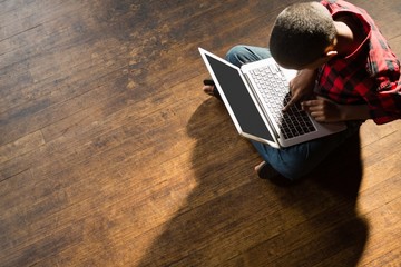 Boy sitting on wooden floor using laptop
