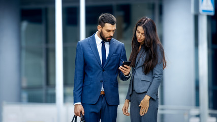 Business Woman and Business Man Use Smartphone and Talk on the Busy Big City Street. Both Look Exquisitely Stylish.