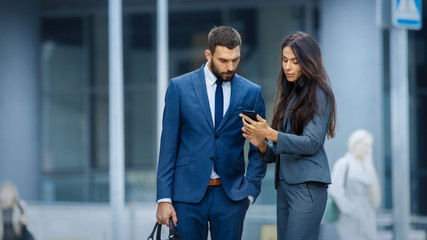 Business Woman and Business Man Use Smartphone and Talk on the Busy Big City Street. Both Look Exquisitely Stylish.