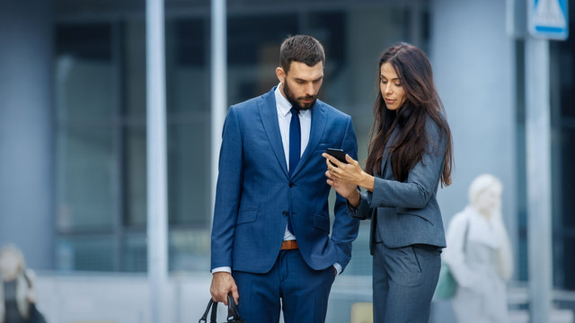 Business Woman and Business Man Use Smartphone and Talk on the Busy Big City Street. Both Look Exquisitely Stylish.