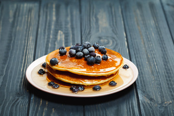 Pancakes with honey and blueberries on wooden table