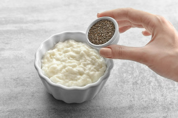 Woman adding chia seeds to pudding on table