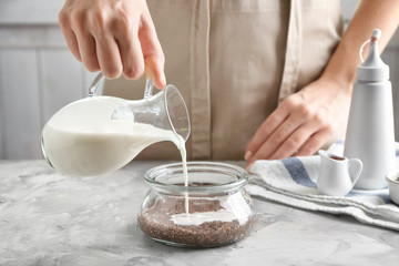 Woman pouring yogurt into glass jar with chia seeds in kitchen