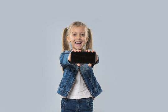 Beautiful Little Girl Hold Cell Smart Phone Empty Screen Happy Smiling Wear Jeans Coat Isolated Over Gray Background