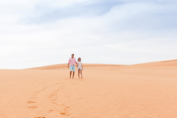 Fototapeta na wymiar Young Man Woman Walking In Desert Couple Girl And Man Hold Hands Sand Dune Landscape Nature Background