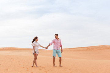 Fototapeta na wymiar Young Man Woman Walking In Desert Couple Girl And Man Hold Hands Sand Dune Landscape Nature Background