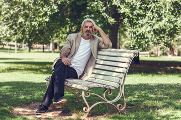 Fototapeta premium Pensive mature man sitting on bench in an urban park.