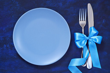 Festive table setting with Christmas ornaments Christmas tree branches, toys and a blue satin bow and ribbon, Plate and Cutlery