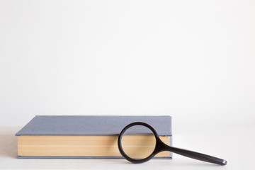 Old book and magnifying glass on the table. Education concept. Empty place for a text. Mock up for different ideas.