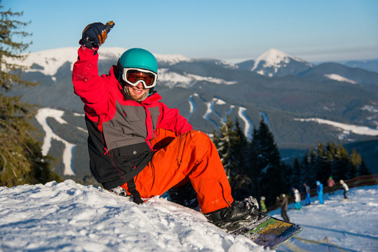 Happy male snowboarder smiling showing thumbs up sitting on the snow in the mountains resting after riding copyspace happiness recreation winter sports resort leisure lifestyle