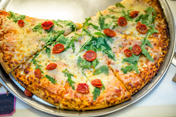 Pizza with arugula and tomatoes is on the shop window in the store