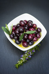 Olives in bowl and rosemary on black background