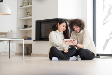 multiethnic couple using tablet computer in front of fireplace
